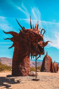 Sculpture on sand at beach against blue sky