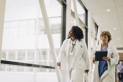 Mature female doctors walking by window in corridor at hospital