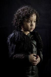 Cute boy looking away while standing against black background