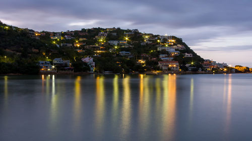 Illuminated buildings by sea against sky