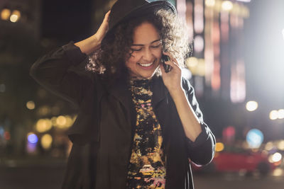 Happy young woman answering smart phone in city at night