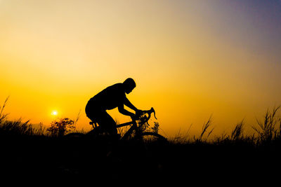 Silhouette young man riding bicycle on field against sky during sunset