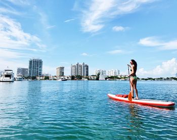 Woman paddleboarding on sea against blue sky