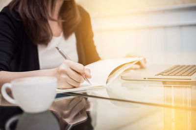 Midsection of woman holding coffee cup on table