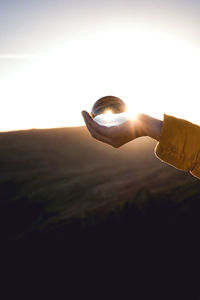 Hand holding sun against sky during sunset