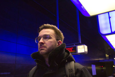 Portrait of young man standing against illuminated wall