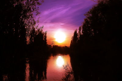 Silhouette trees by lake against sky during sunset