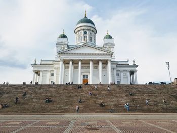 People of n steps outside cathedral against cloudy sky