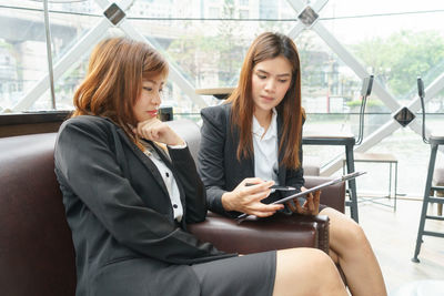 Young woman using mobile phone while sitting on window