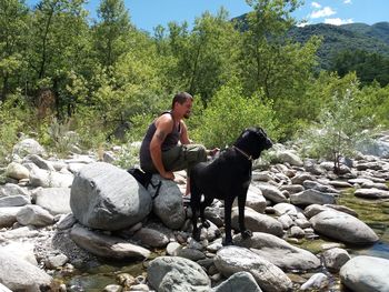 Full length of man with dog sitting on rock at forest