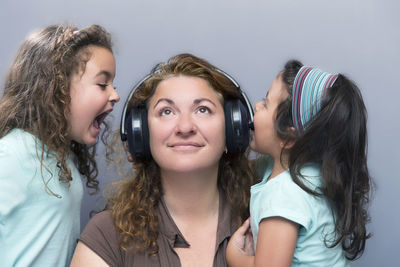 Daughters shouting amidst mother wearing headphones by wall