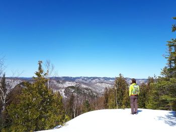 Rear view of woman looking at landscape while standing on snow against clear blue sky