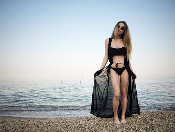 Portrait of sensuous woman standing at beach against sky