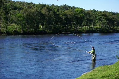 Man fishing in lake against trees