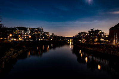 Illuminated buildings by river against sky at night