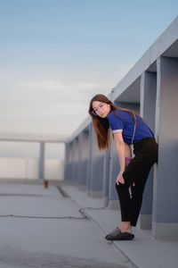 Portrait of young woman standing by railing against sky