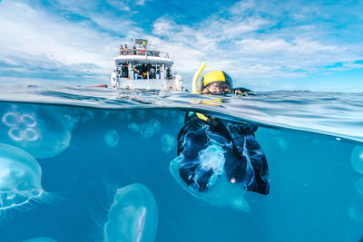 A woman in a black wetsuit is in the water with jellyfish. the jellyfish are floating around her