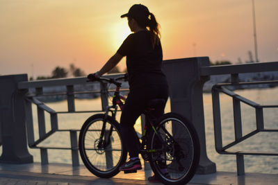 Man riding bicycle on railing against sky during sunset