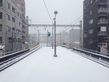 Snow covered railroad tracks by buildings in city
