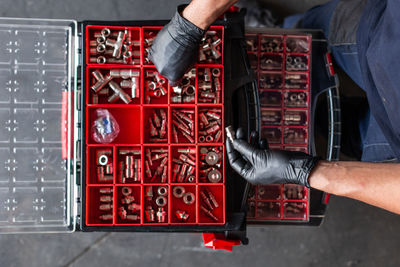 Top view of anonymous mechanic in gloves sorting various nuts and screws inside tool box during work in garage