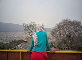 Rear view of woman standing by bare tree against clear sky