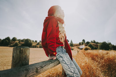 Side view of woman sitting on railing against clear sky during sunny day