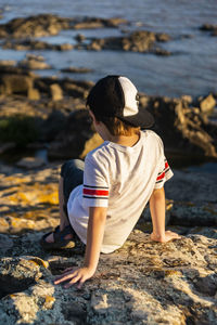 Rear view of boy on rock at beach