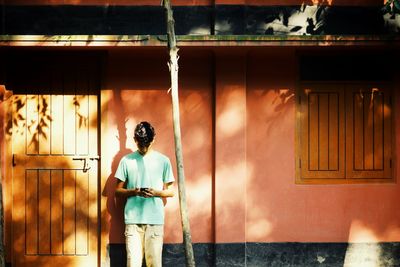 Boy using mobile phone while standing against wall outdoors