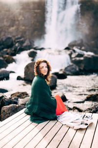 Portrait of woman sitting on rock by water