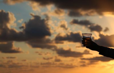 Close-up of hand holding silhouette chain against sky during sunset