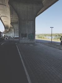 Empty road below bridge against sky