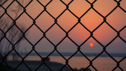 Full frame shot of chainlink fence against sky during sunset