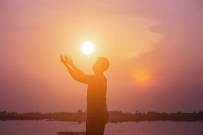 Silhouette man standing by lake against sky during sunset