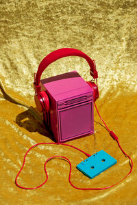 From above of vintage pink stereo speaker in headset connected to audio tape placed on yellow textile in studio