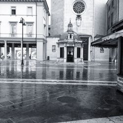 Wet street by buildings in city