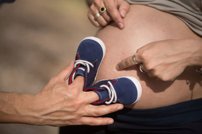 Cropped hand of man holding shoes on pregnant woman belly