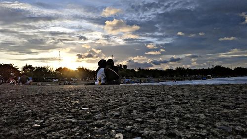 Rear view of woman walking on beach against sky during sunset