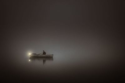 Man sitting on rowboat in sea during dusk