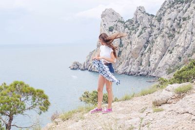 Rear view of woman on rock by sea against sky