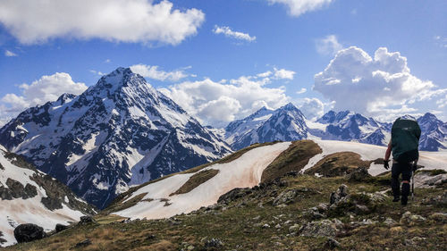 Rear view of hiker walking on mountain against sky