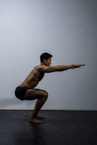 Shirtless muscular man exercising against wall