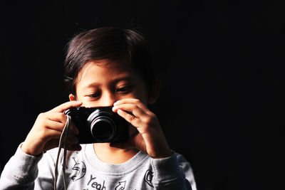 Portrait of teenage girl photographing against black background