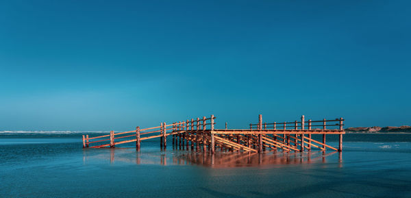 Pier over sea against clear blue sky