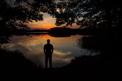 Silhouette man standing by lake against sky during sunset