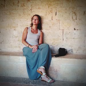 Full length of thoughtful woman sitting against wall