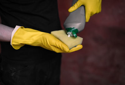 Caucasian male builder in yellow gloves squeezes detergent onto a sponge.