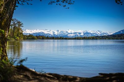 Scenic view of lake and mountains against clear blue sky