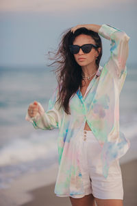 Portrait of young woman wearing sunglasses standing at beach