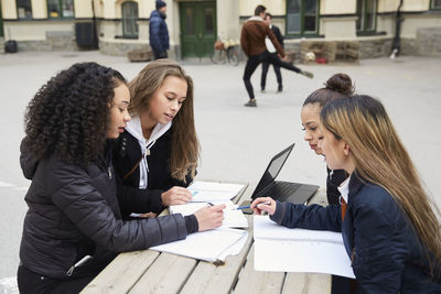 Multi-ethnic female teenage friends studying at table in schoolyard