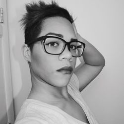 Close-up portrait of young woman wearing eyeglasses by wall